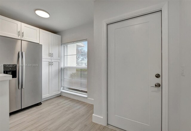 kitchen with light wood-style flooring, stainless steel fridge, light countertops, and white cabinets