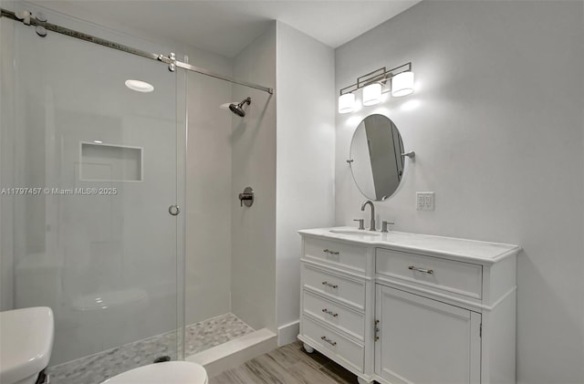 full bathroom featuring toilet, wood finished floors, vanity, a shower stall, and baseboards
