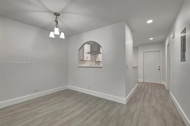 empty room featuring light wood finished floors, a sink, electric panel, baseboards, and recessed lighting