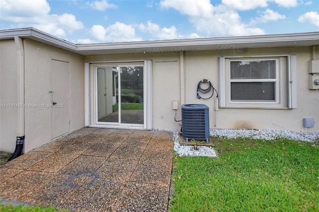 entrance to property featuring a yard, stucco siding, a patio area, and central AC