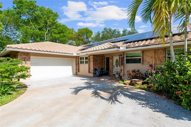 single story home with brick siding, a garage, a tile roof, concrete driveway, and roof mounted solar panels