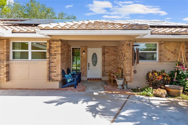 property entrance featuring brick siding, a tile roof, and roof mounted solar panels