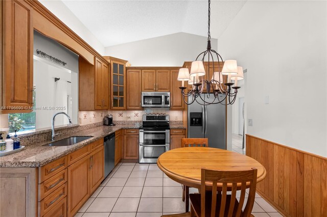 kitchen with a sink, lofted ceiling, brown cabinets, an inviting chandelier, and appliances with stainless steel finishes