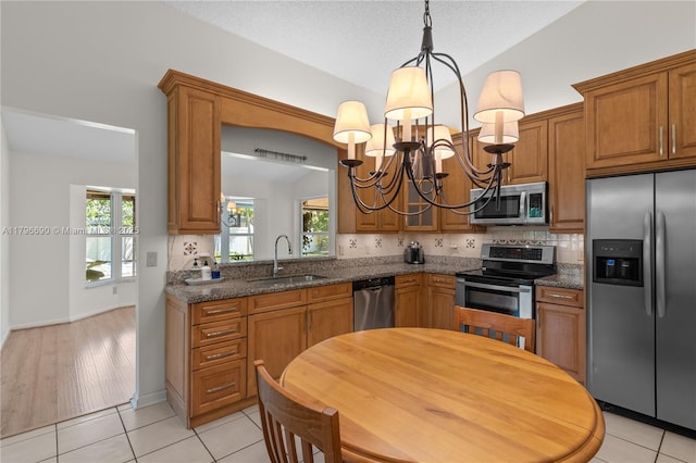 kitchen with a sink, a chandelier, brown cabinets, stainless steel appliances, and tasteful backsplash