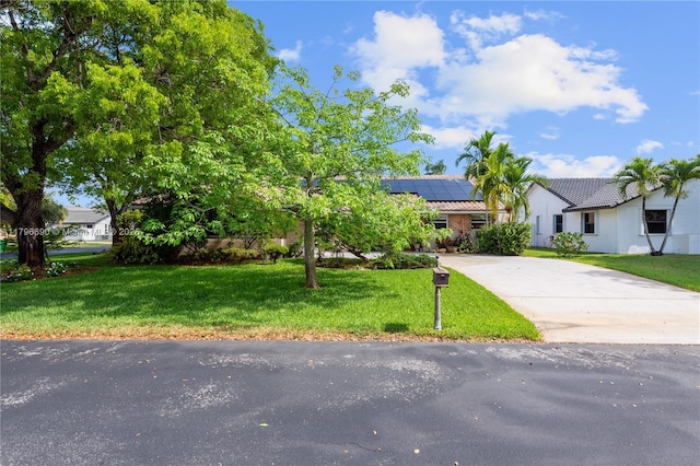 view of front facade with a tiled roof, stucco siding, solar panels, a front yard, and driveway