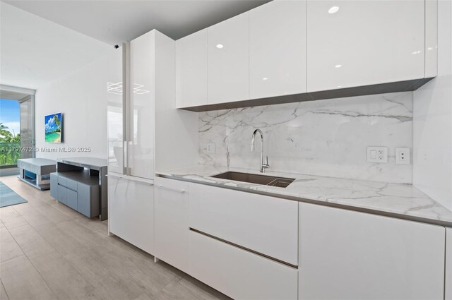 10201 Collins Ave Unit 303, Bal Harbour, FL 33154 - kitchen featuring modern cabinets, white cabinetry, a sink, decorative backsplash, and light stone counters