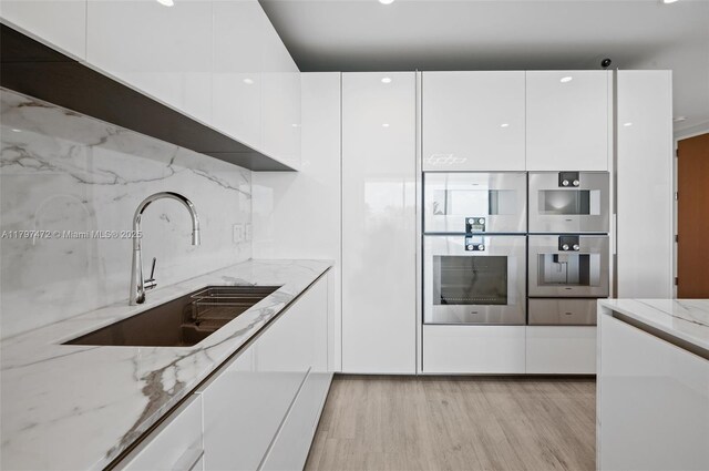 10201 Collins Ave Unit 303, Bal Harbour, FL 33154 - kitchen with modern cabinets, a sink, white cabinetry, and light wood-type flooring