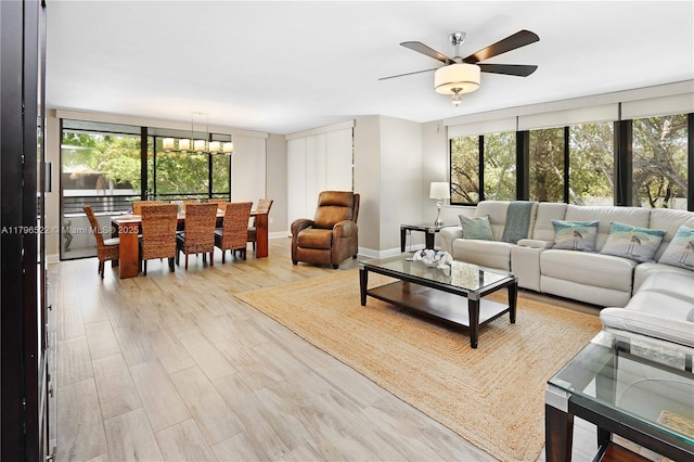 living area with baseboards, a ceiling fan, a healthy amount of sunlight, and light wood-style floors