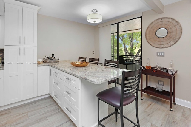 kitchen featuring light stone countertops, a peninsula, a kitchen breakfast bar, and light wood finished floors