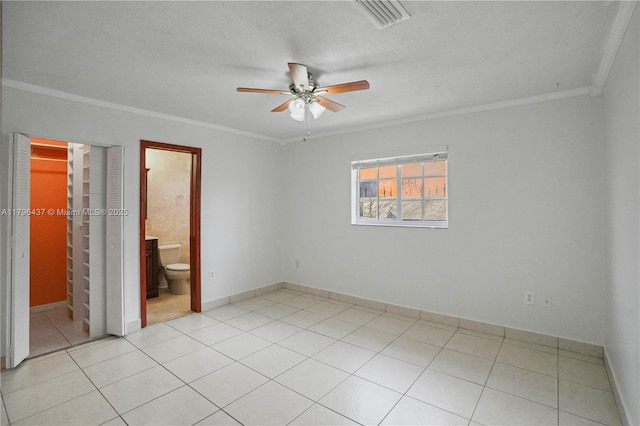 unfurnished bedroom featuring a walk in closet, light tile patterned flooring, crown molding, and visible vents