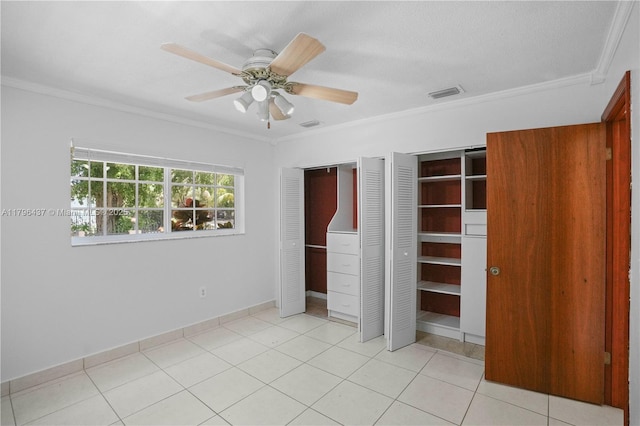 unfurnished bedroom featuring light tile patterned floors, ornamental molding, ceiling fan, visible vents, and multiple closets