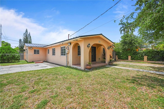 view of front of property with fence, a patio, stucco siding, a front yard, and a standing seam roof