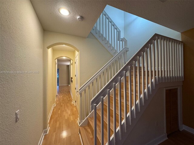 8706 Blaze Ct, Davie, FL 33328 - staircase featuring a textured wall, a textured ceiling, wood finished floors, arched walkways, and baseboards