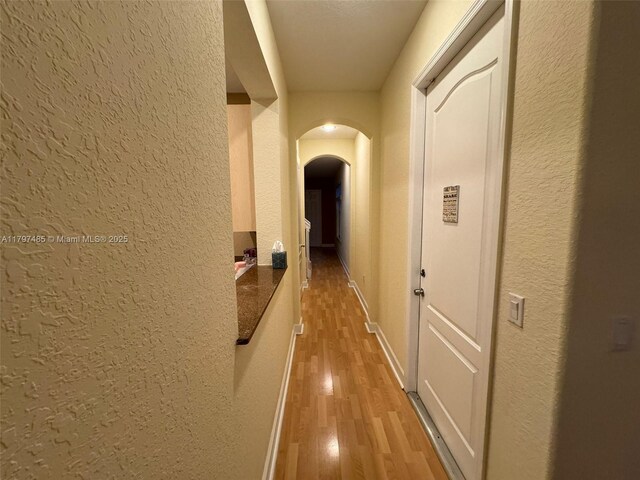 8706 Blaze Ct, Davie, FL 33328 - hallway with a textured wall, arched walkways, light wood-style floors, and baseboards