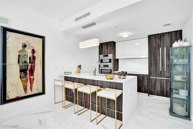 kitchen featuring marble finish floor, modern cabinets, visible vents, a kitchen bar, and double oven