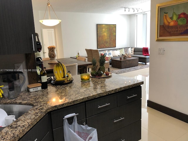 kitchen featuring dark cabinets, rail lighting, pendant lighting, and stone countertops