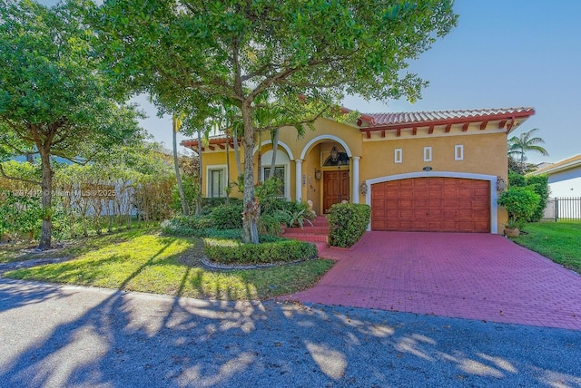 mediterranean / spanish house with fence, decorative driveway, stucco siding, a tile roof, and a front yard