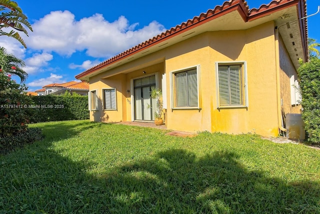 back of property featuring a yard, a tile roof, stucco siding, and central air condition unit