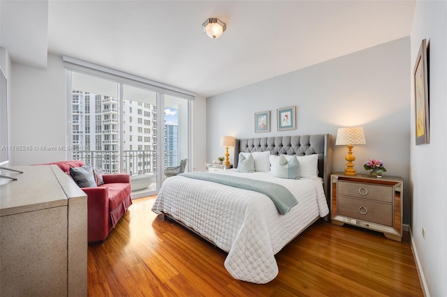 bedroom with baseboards, access to outside, floor to ceiling windows, and wood finished floors