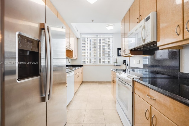 kitchen featuring a sink, white appliances, dark stone countertops, light tile patterned floors, and baseboards