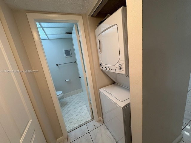 laundry area with laundry area, a textured ceiling, and stacked washer and dryer