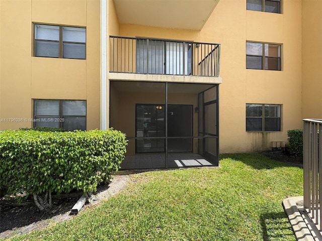 back of property with a yard, stucco siding, and a balcony