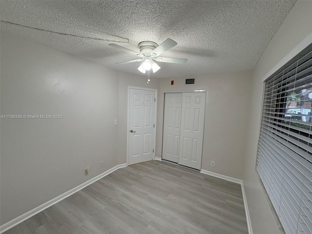 unfurnished bedroom featuring wood finished floors, a textured ceiling, visible vents, ceiling fan, and baseboards