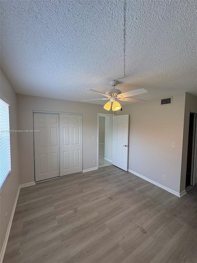 unfurnished bedroom with a closet, visible vents, wood finished floors, and baseboards