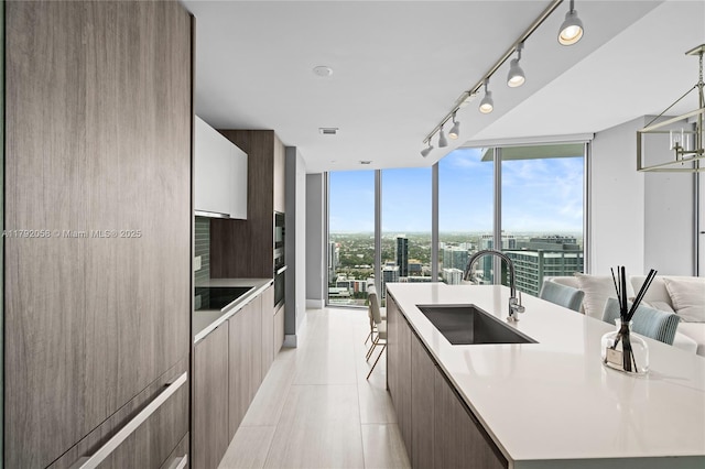 kitchen with a sink, light countertops, modern cabinets, and a center island with sink