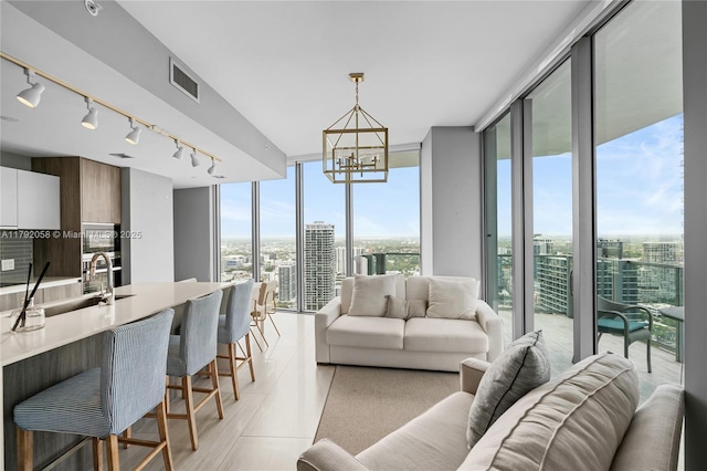 living area featuring light tile patterned floors, a wall of windows, rail lighting, visible vents, and a chandelier