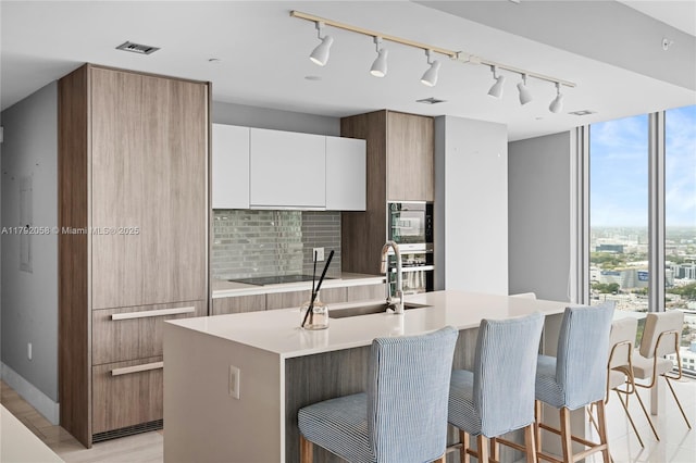 kitchen with black electric cooktop, modern cabinets, a kitchen bar, and a sink