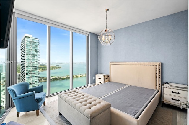 bedroom featuring expansive windows, a water view, a notable chandelier, and wood finished floors