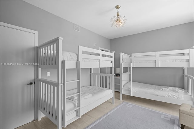 bedroom with an inviting chandelier, visible vents, and wood finished floors