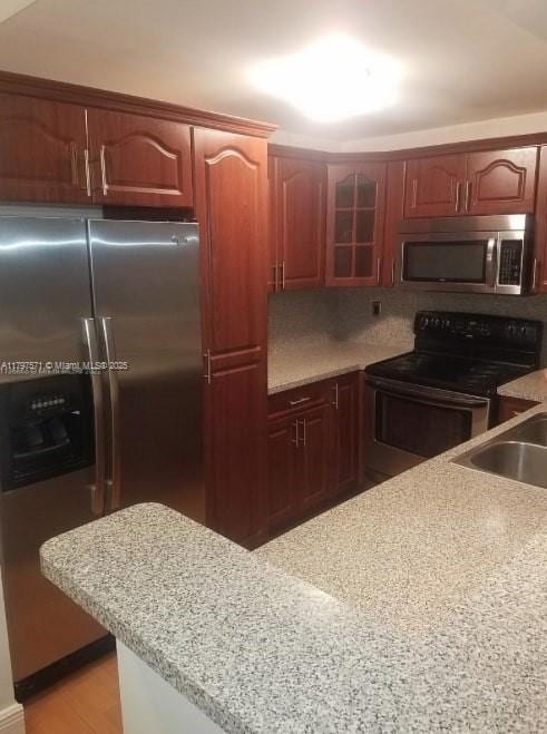 kitchen with light stone countertops, glass insert cabinets, a sink, tasteful backsplash, and appliances with stainless steel finishes