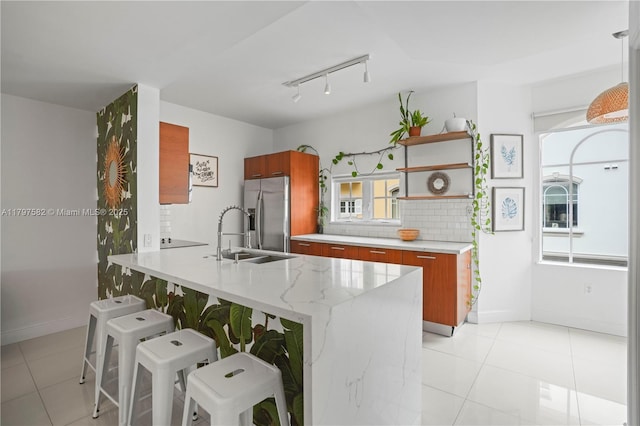 18445 NE 27th Pl, Aventura, FL 33160 - kitchen with a breakfast bar area, brown cabinetry, light tile patterned floors, a sink, and stainless steel refrigerator with ice dispenser