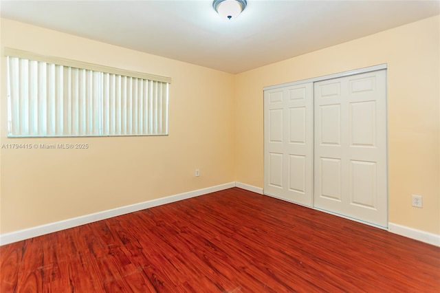 unfurnished bedroom featuring a closet, dark wood finished floors, and baseboards