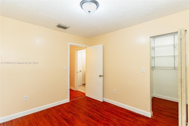 unfurnished bedroom featuring a closet, baseboards, visible vents, wood finished floors, and a spacious closet
