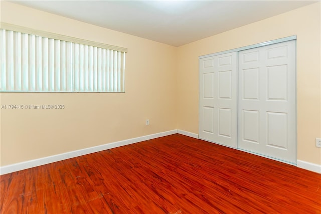unfurnished bedroom with baseboards, dark wood finished floors, and a closet