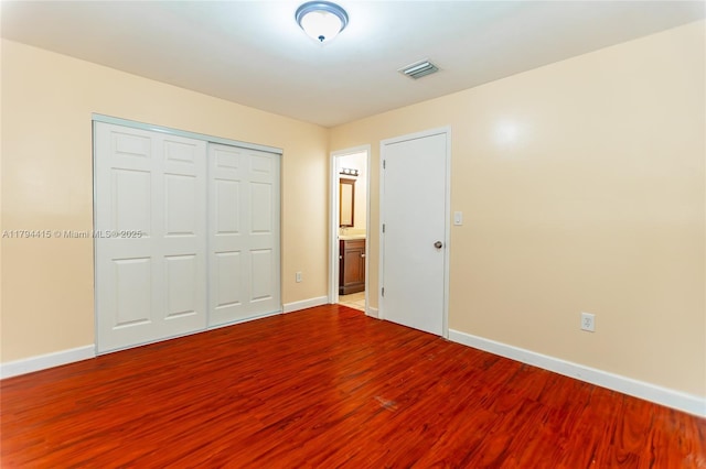 unfurnished bedroom featuring baseboards, a closet, visible vents, and wood finished floors