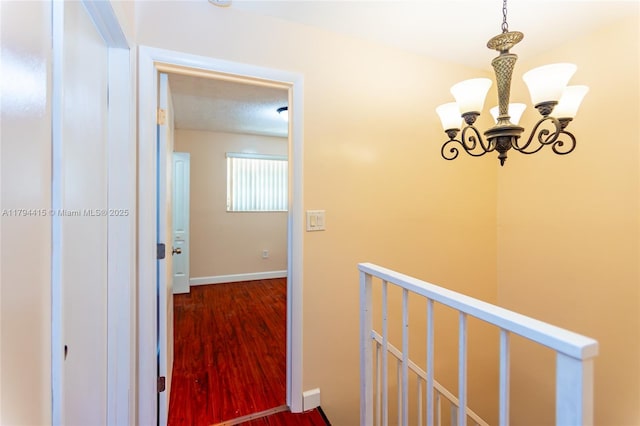 hallway featuring a chandelier, baseboards, an upstairs landing, and wood finished floors