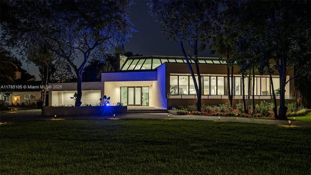 back of house at night featuring a yard and stucco siding