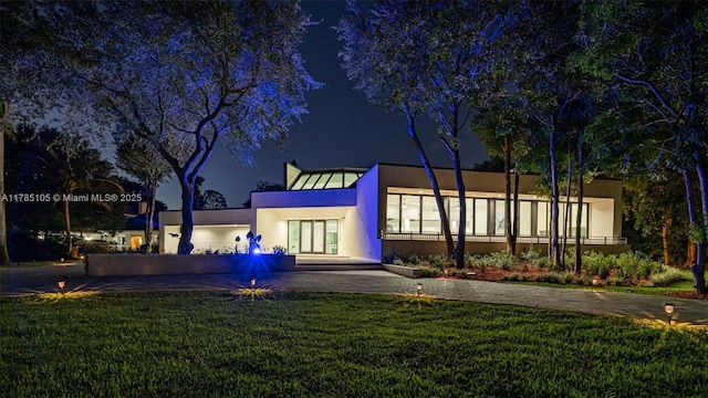 back of house at twilight featuring a lawn, a standing seam roof, stucco siding, and metal roof