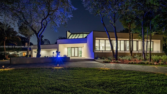 back of house at night featuring a yard and stucco siding