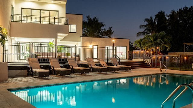 pool at night with a patio, a fenced in pool, and fence