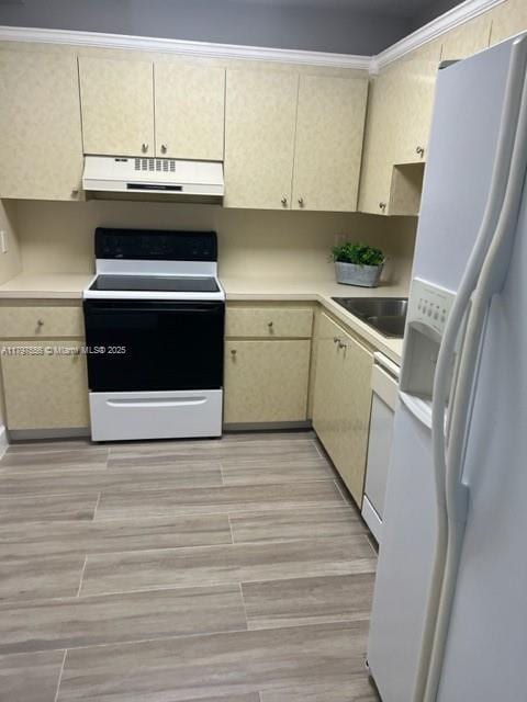 kitchen featuring cream cabinets, a sink, white appliances, under cabinet range hood, and light countertops
