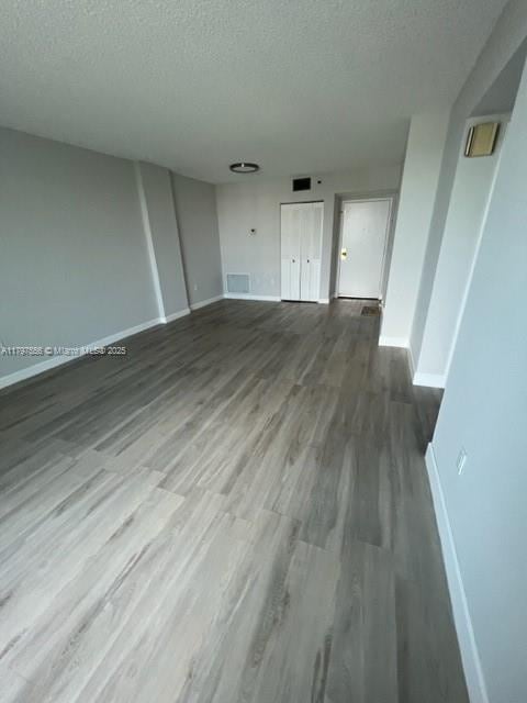 empty room featuring a textured ceiling, visible vents, baseboards, and wood finished floors