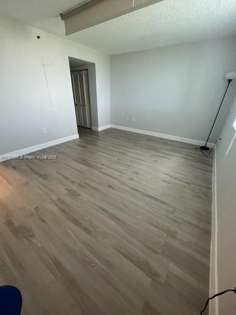 unfurnished room with a textured ceiling, wood finished floors, and baseboards