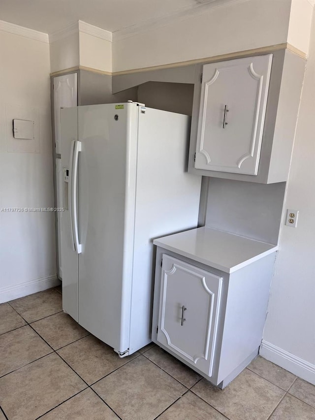 kitchen featuring ornamental molding, light countertops, light tile patterned floors, white refrigerator with ice dispenser, and baseboards