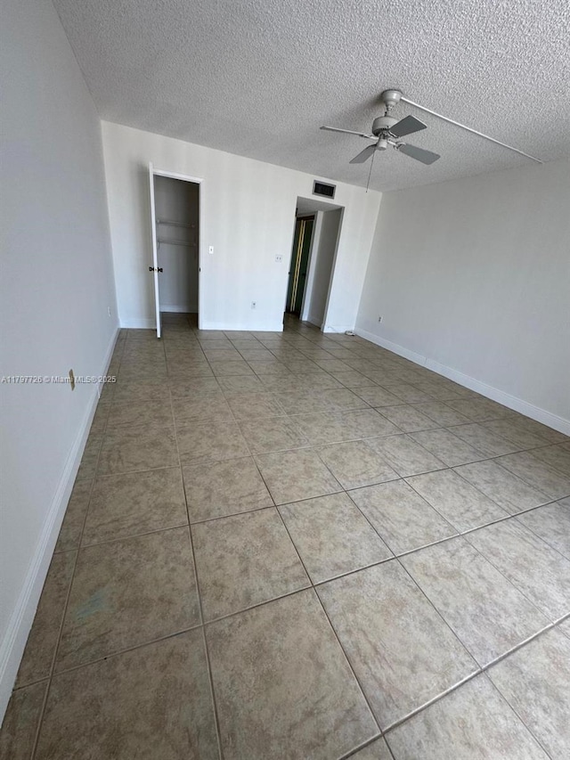 tiled spare room with baseboards, ceiling fan, visible vents, and a textured ceiling