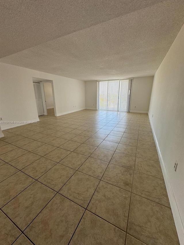 empty room with a textured ceiling, baseboards, and light tile patterned flooring